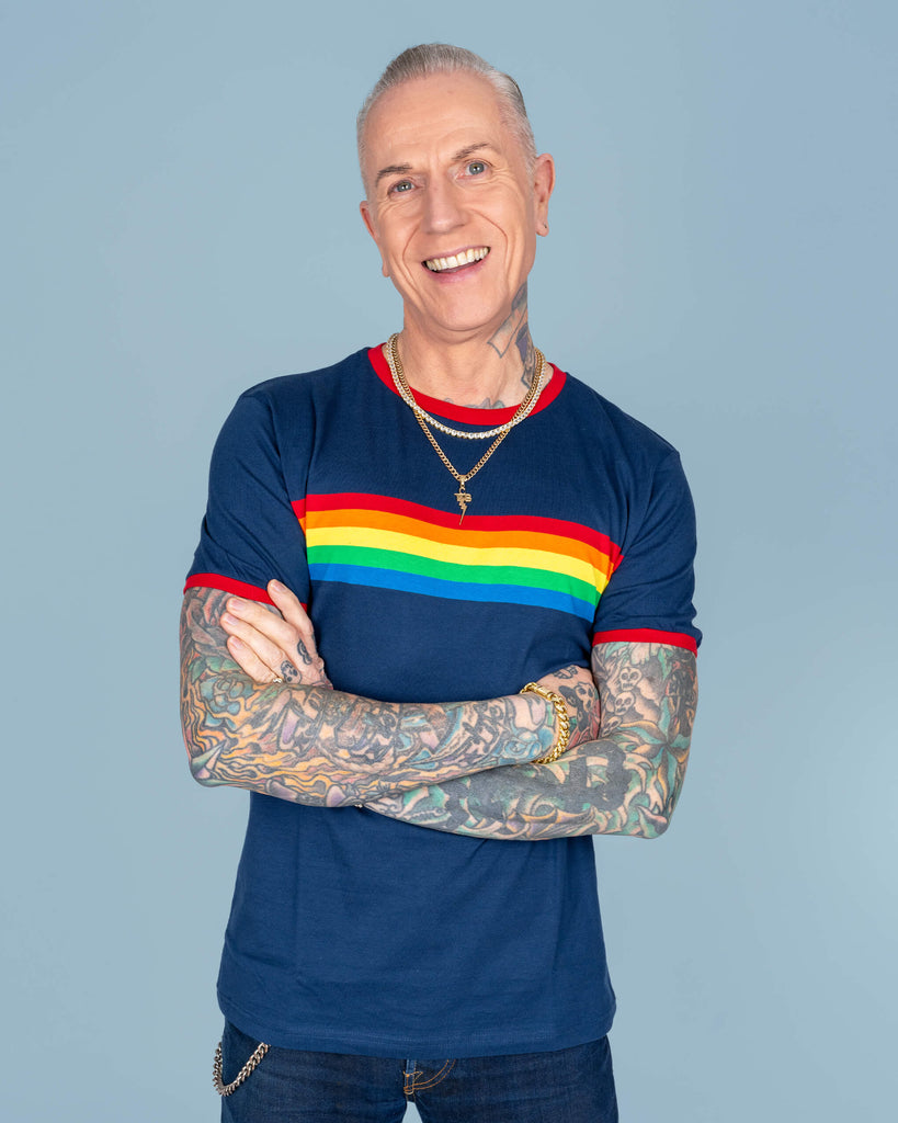 James smiles confidently while modelling the navy rainbow t-shirt, showcasing the flattering fit and colourful stripe detail. His tattooed arms and gold jewellery add an edgy touch to the vibrant design.