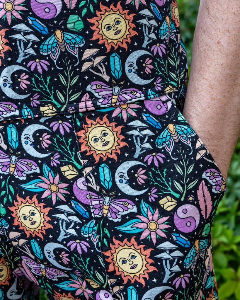 Close-up of Run & Fly’s “Boho Summer” print, designed by Waffle Mama. The vibrant pattern includes sun faces, moons, flowers, and butterflies. Jack’s hand rests in the pocket of the dungarees, highlighting the intricate and colourful design.