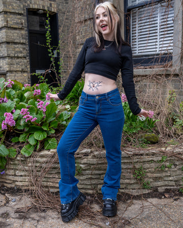 Model smiling and posing outdoors in slim fit stonewash stretch denim bootcut jeans and a black crop top.
