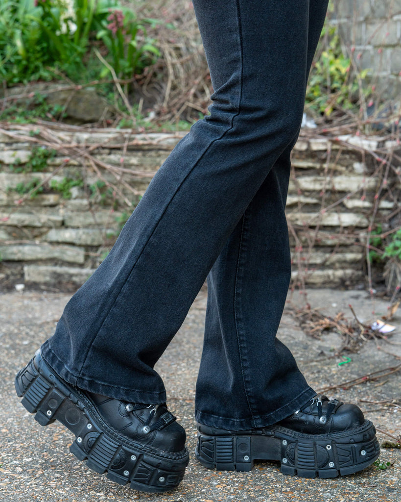 Close-up of the hem and boots showing the flare of Run & Fly Black Stretch Denim Slim Bootcut Jeans. The jeans fall neatly over chunky black platform shoes. Ethical slow fashion design in comfortable stretch denim.