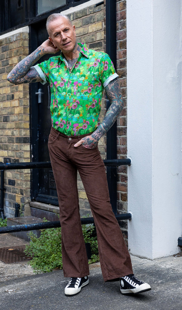 James a tattooed white male with silver hair in his 50's is posing wearing a frog print shirt and brown corduroy flares stood in a mews in Hove UK