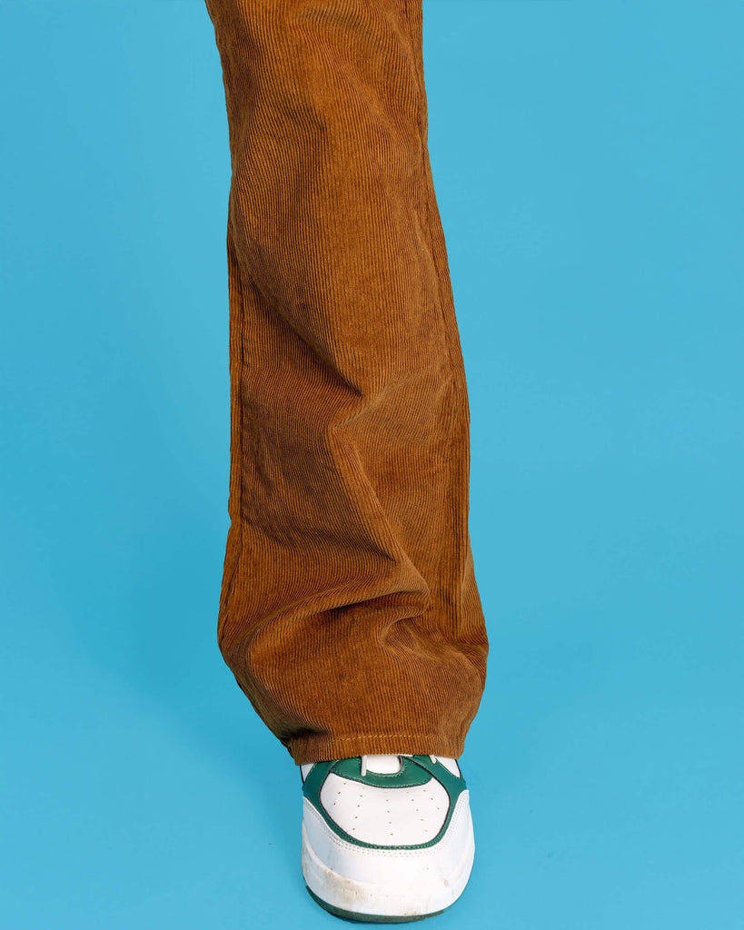 Close up shot of the tobacco cord bootcut flares in front of a blue studio background, cropped in on the flare over a white trainer.