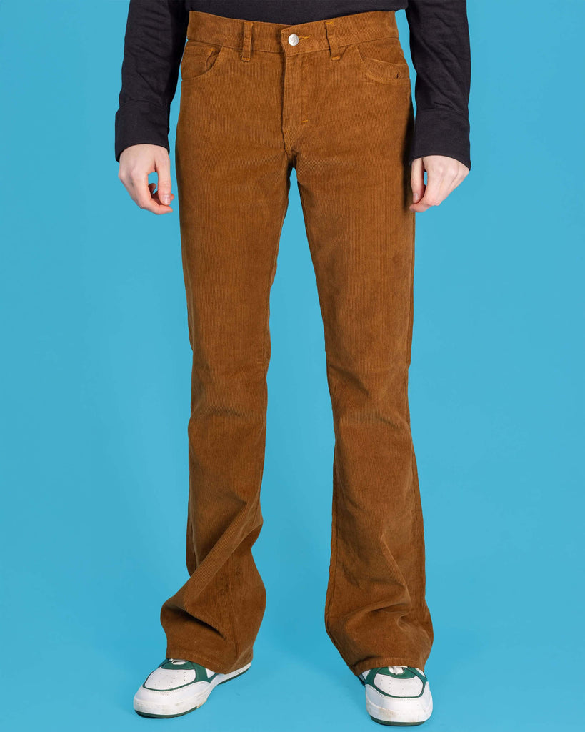 Jack is stood in front of a blue studio background wearing the tobacco cord bootcut flares with a long sleeve black tshirt and white trainers. They are facing forward with both arms resting by their sides. Photo is cropped from the waist down.