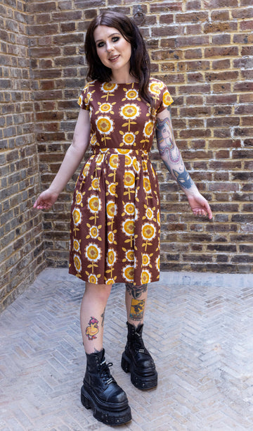 Florence a brown long haired white model with tattoos is wearing a brown retro tea dress with floral print against a brick wall