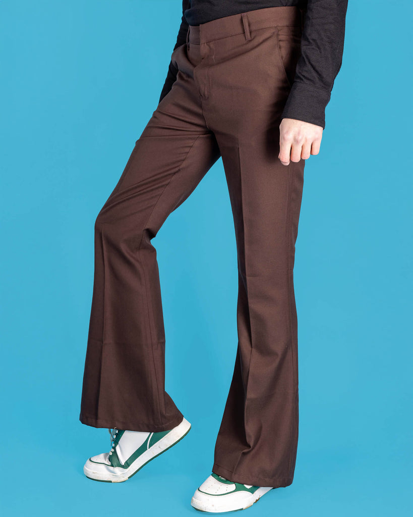 Jack is stood in front of a blue studio background wearing the Presley brown bell bottom trouser slacks with a long sleeve black tshirt and white trainers. They are facing the left and posing with one leg bent forward to highlight the flares. Photo is cropped from the waist down.