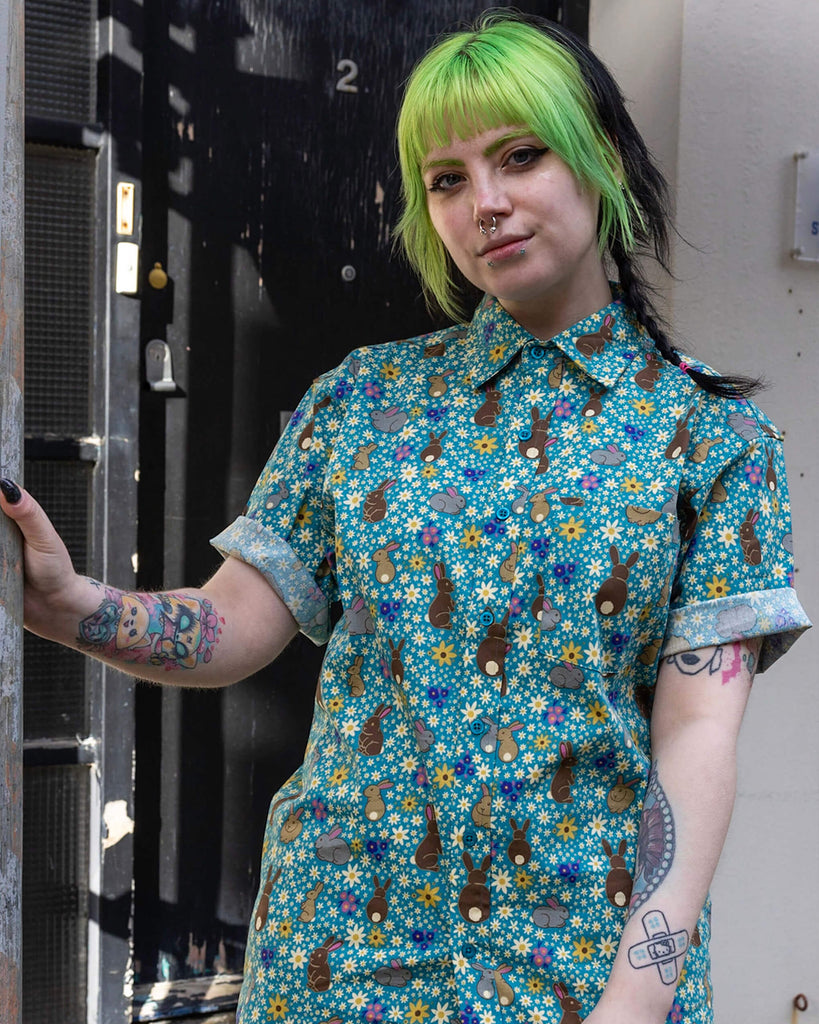 Faeryn is wearing the Bunny Meadow short sleeve blue shirt with floral pattern, worn with black corduroy stretch flare trousers. Model is looking at the camera.
