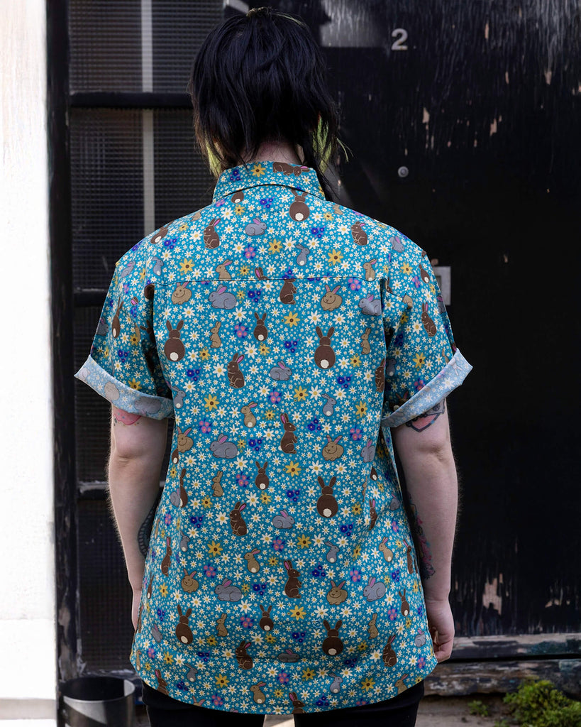 Faeryn is wearing the Bunny Meadow short sleeve blue shirt with floral pattern, worn with black corduroy stretch flare trousers. Model has back to the camera the camera.