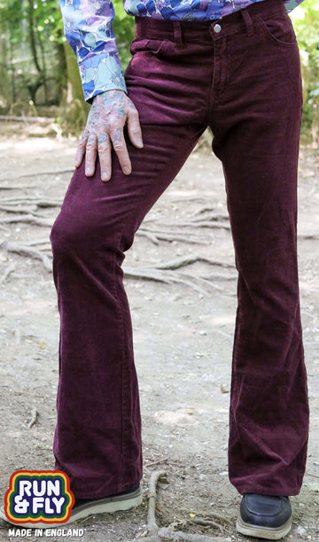 Model is stood in a forest area wearing the Burgundy boot cut flare cords with a purple floral shirt and brown boat shoes. The model is facing the camera posing with one leg out to the side to show off the flares with one hand on his thigh and the other behind his back. Photo is cropped from the waist down.