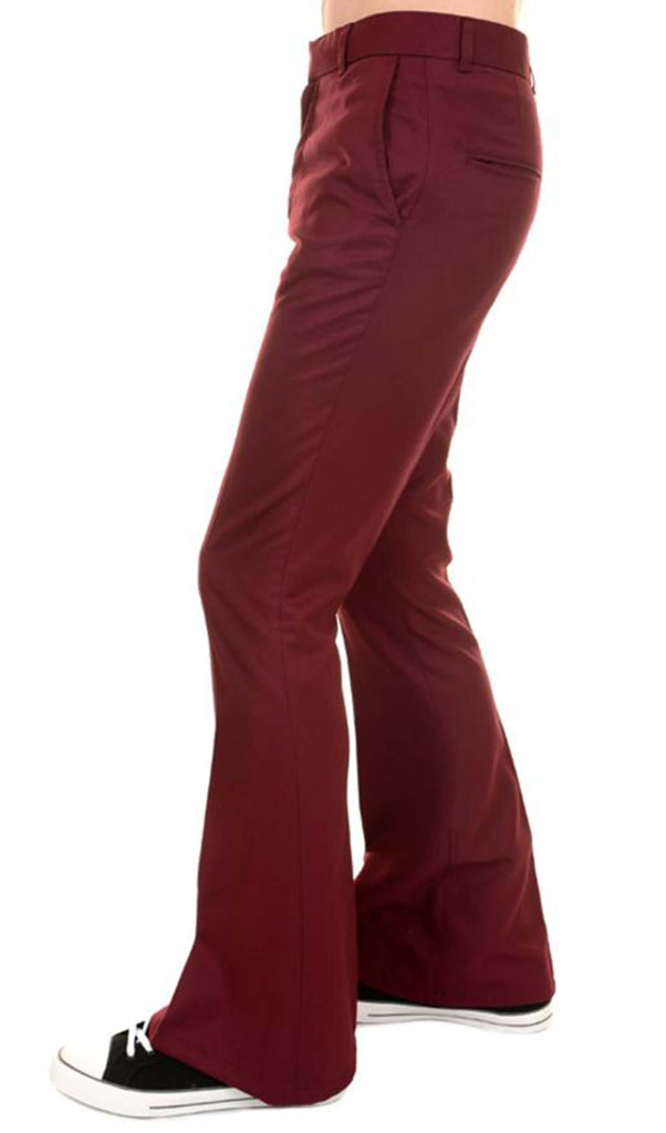Model is stood in front of a white studio background wearing the Presley burgundy bell bottom trouser slacks with black trainers. They are facing to the left with one leg bent forward to highlight the flares. Photo is cropped from the waist down.