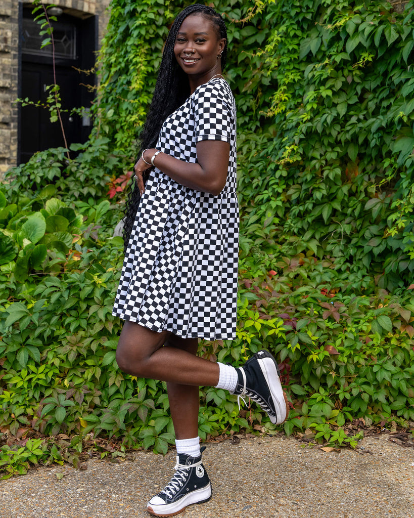 The model strikes a playful pose in a black and white checkered dress from Run & Fly. The knee-length dress with a loose silhouette is paired with black platform trainers and white socks. The backdrop of green leaves adds to the slow fashion narrative of the brand.