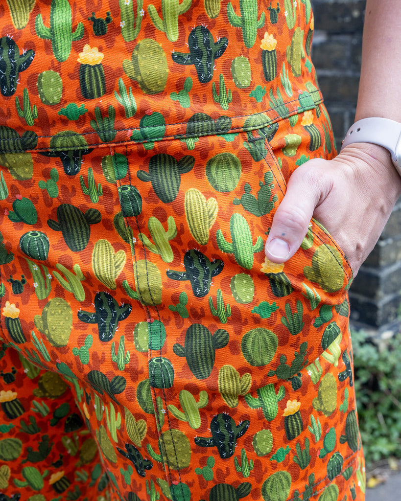 close up of Cactus Stretch Twill Dungarees. Close up shows the model's hand in the pocket of the dungarees. The photo is taken outdoors in Hove.
