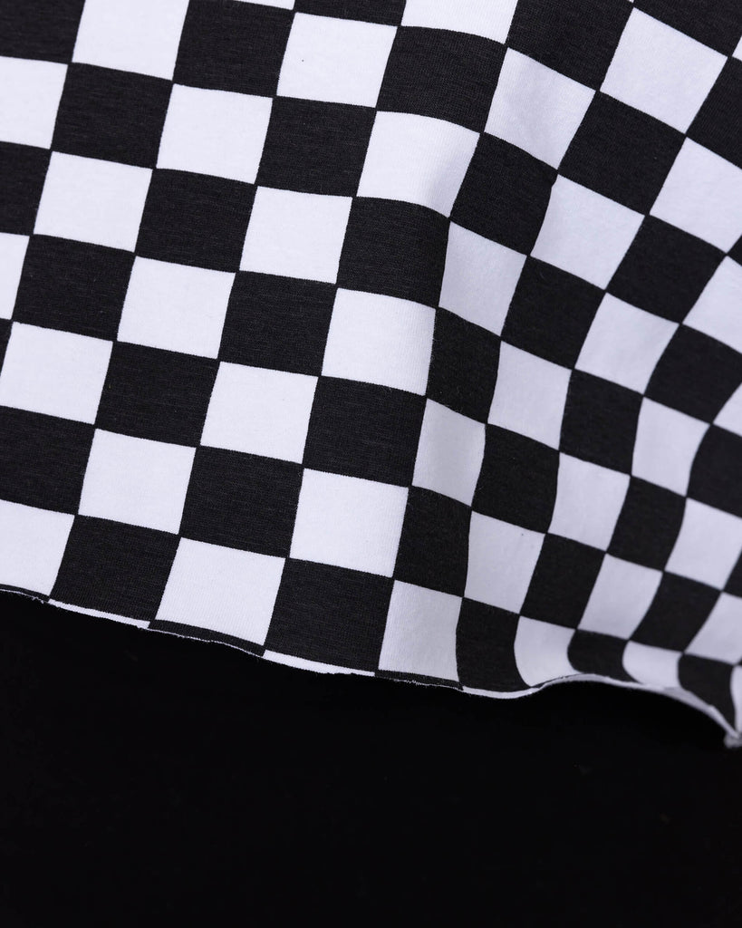 Close up of the Checkerboard Short Sleeve Crop Tee worn by a femme model with high rise black leggings in front of a white studio background. The crop tee has an all over black and white checkerboard print with a raw hem for a y2k 90s style.