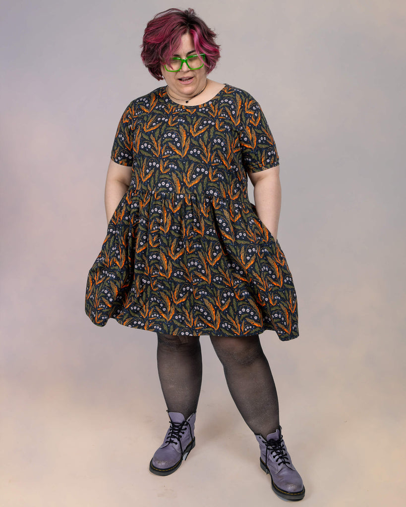 Jackie Brand playfully poses in the Run & Fly smock dress with side pockets. The bold botanical skull design by Clare Lewis adds a spooky charm to the comfortable, loose-fit style.