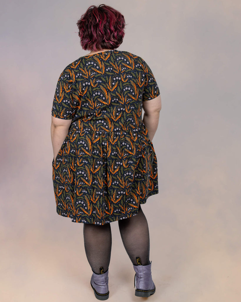  Back view of Jackie Brand in the Run & Fly smock dress by Clare Lewis. The seamless continuation of the botanical and skull print highlights the playful design against the flowy silhouette.