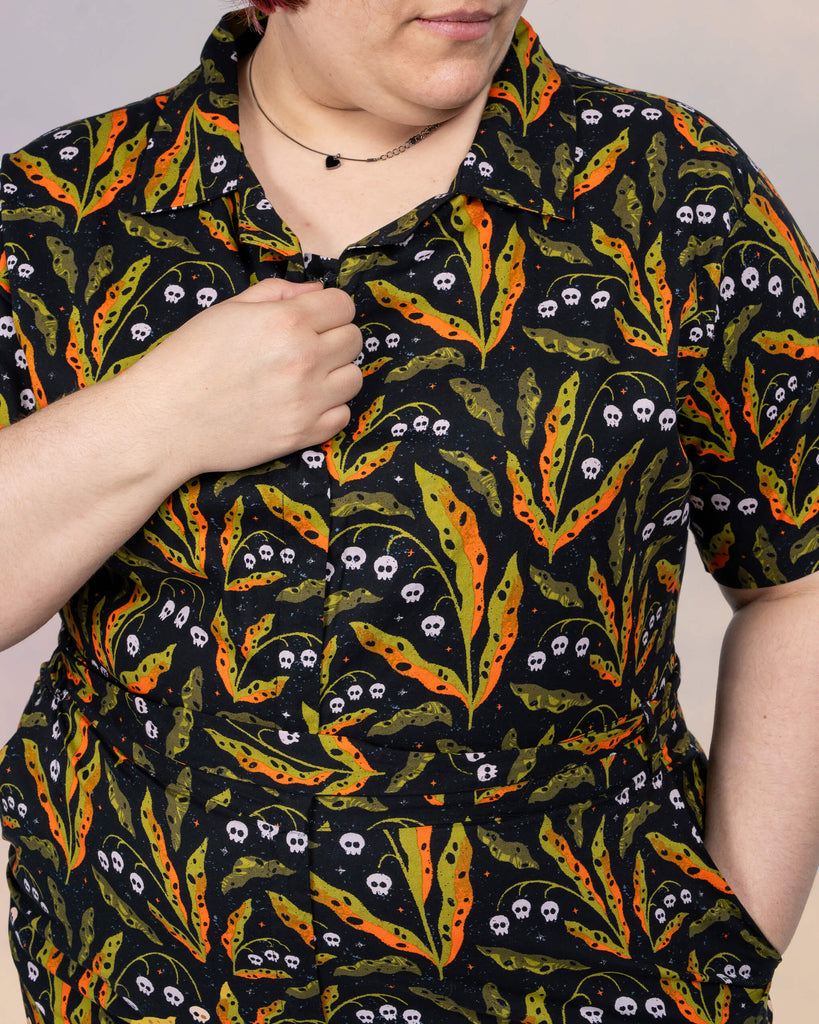 Close-up of Jackie Brand adjusting the collar of the Run & Fly jumpsuit. The design features orange and green leaves with tiny skulls, perfect for autumnal vibes.