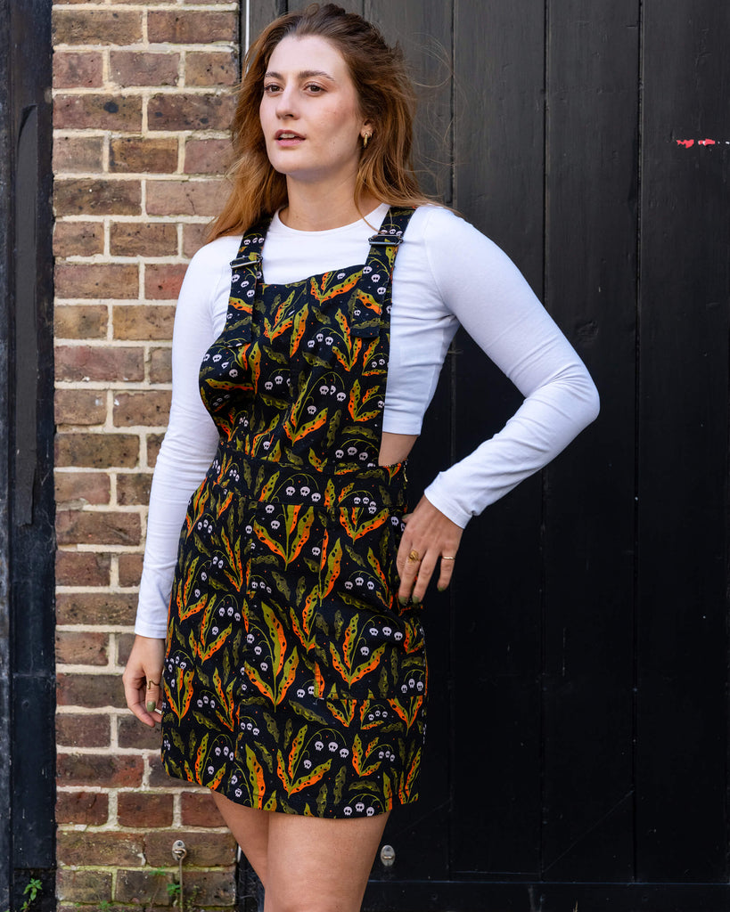 Model wearing Run & Fly’s ethical slow fashion poison pinafore dress with a bold, vibrant pattern featuring skulls and leaves. The small British brand is known for its quirky, eco-friendly designs. Perfect for adding an alternative edge to any outfit.