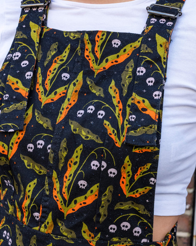 Close-up of Run & Fly’s poison pinafore dress, showcasing its unique skull and leaf print in vibrant orange and green tones. The small British brand is committed to ethical, slow fashion, offering quirky designs with sustainable materials. This dress combines bold style with comfort, perfect for those who love to stand out while supporting eco-friendly fashion.