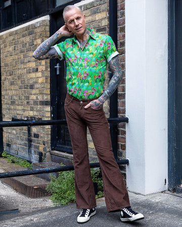James a tattooed white male with silver hair in his 50's is posing wearing a frog print shirt and brown corduroy flares stood in a mews in Hove UK