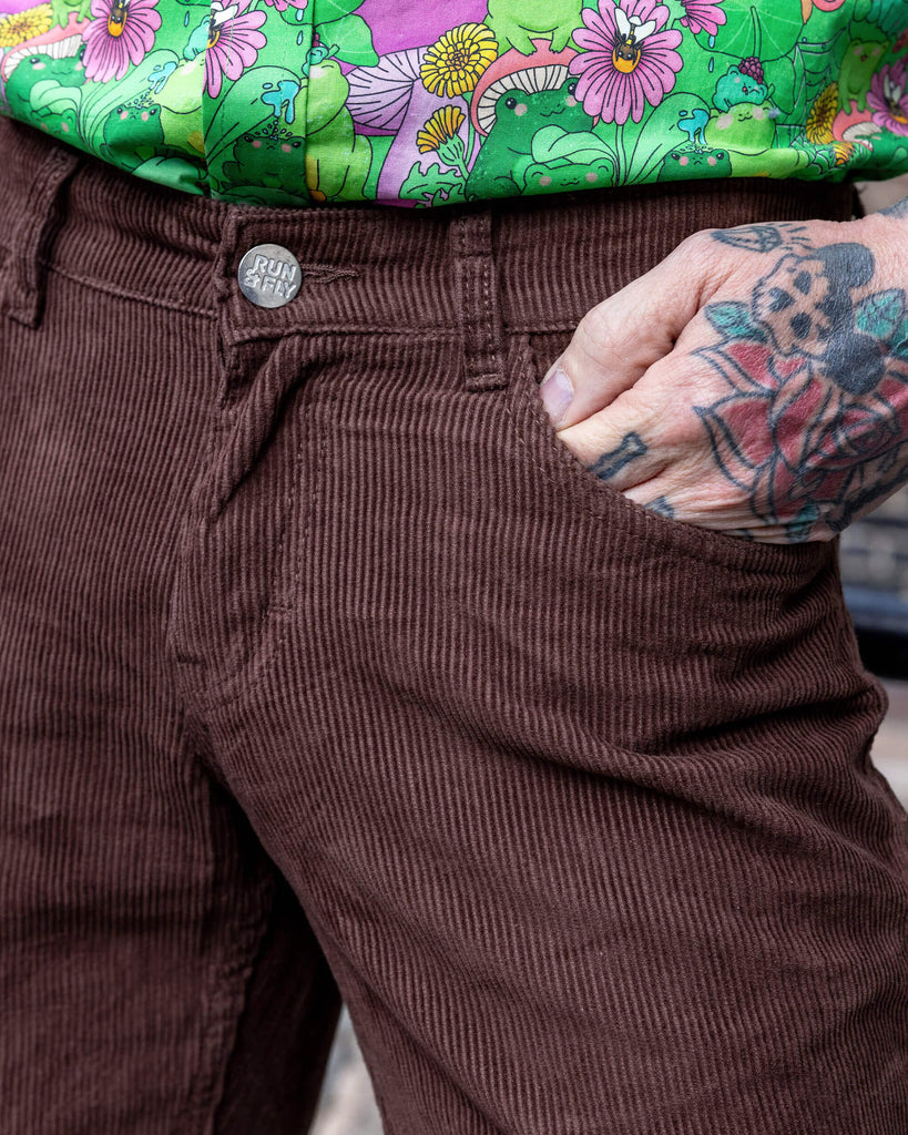 close up of James a tattooed white male with silver hair in his 50's is posing wearing a frog print shirt and brown corduroy flares stood in a mews in Hove UK. He has a hand in his pocket