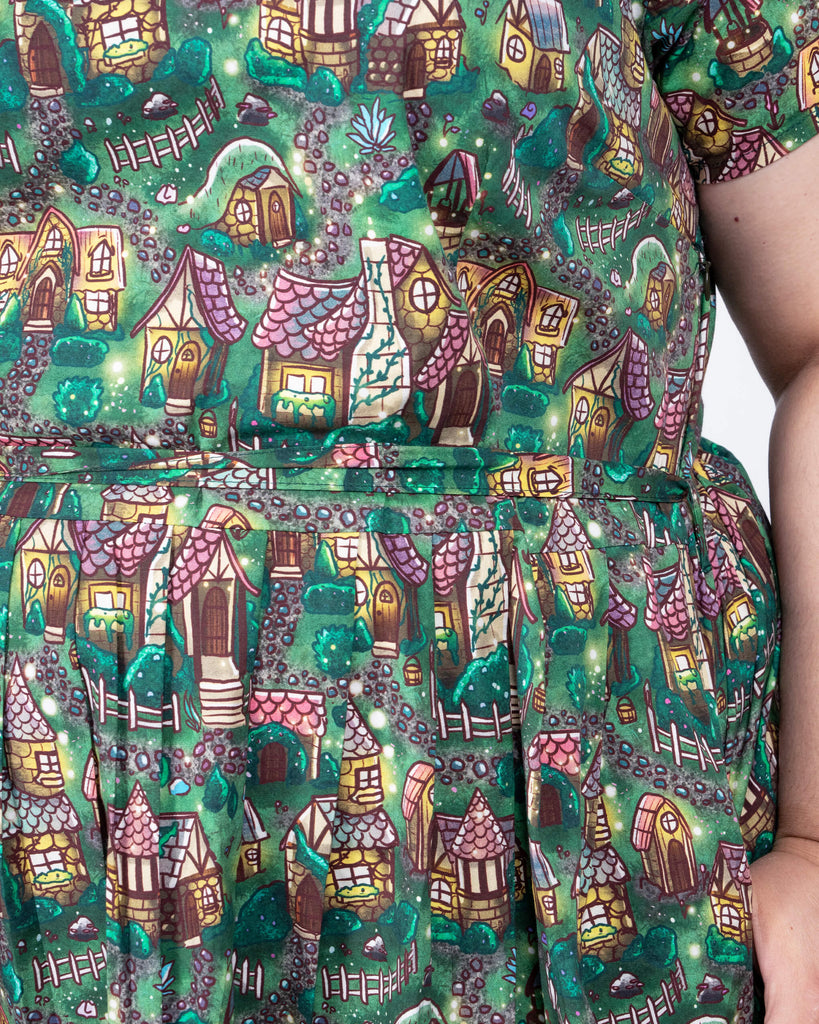 Close-up of the “Cosy Cottage” print by Lauren Ash Design on the Run & Fly tea dress. The pattern features hand-drawn whimsical cottages surrounded by lush greenery and rustic garden elements, adding charm to the outfit.