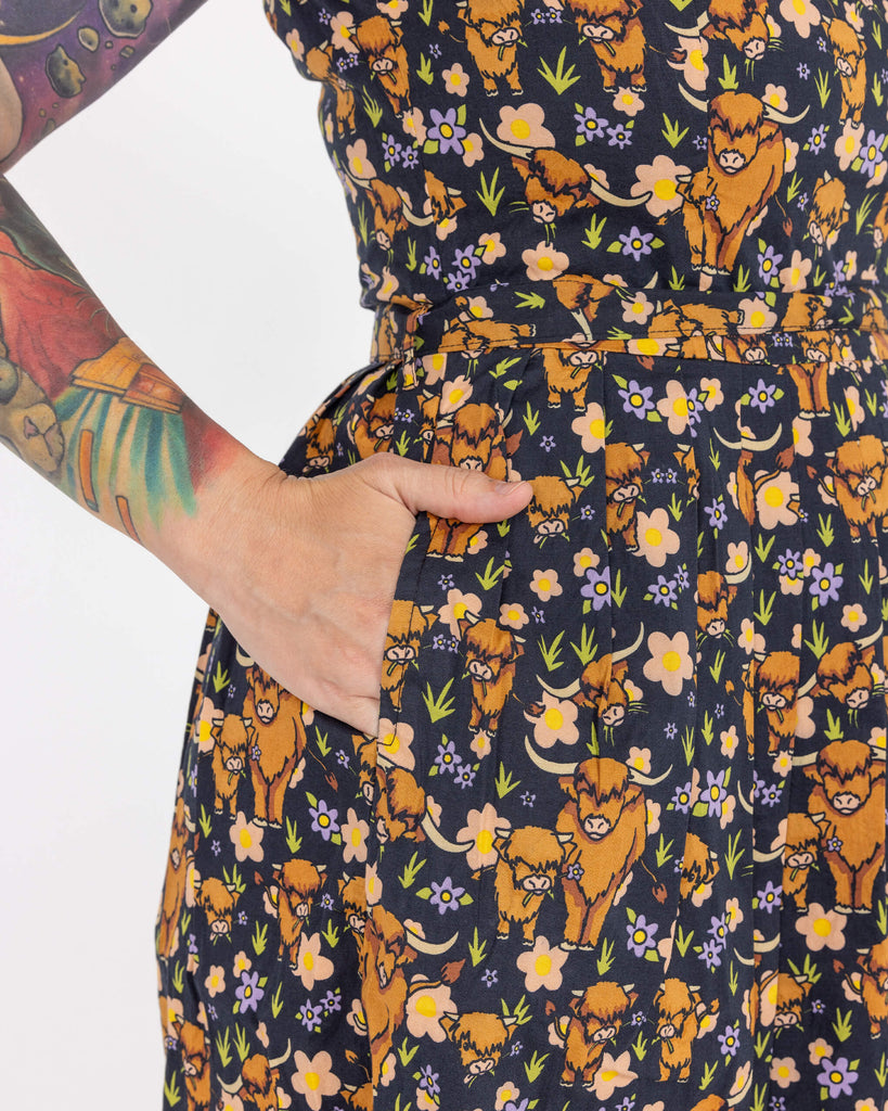 Close up of Laura wearing a highland cow printed tea dress in front of a white background at a studio in Hove. Her hand is in the pocket of the dress.