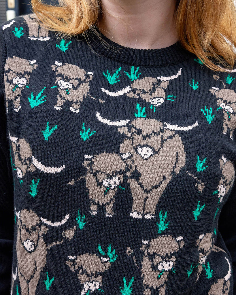 Close up of Florence, a femme model with blonde hair stood outside in Hove wearing Highland Cow Jumper. The jumper is black with highland cows on the torso.