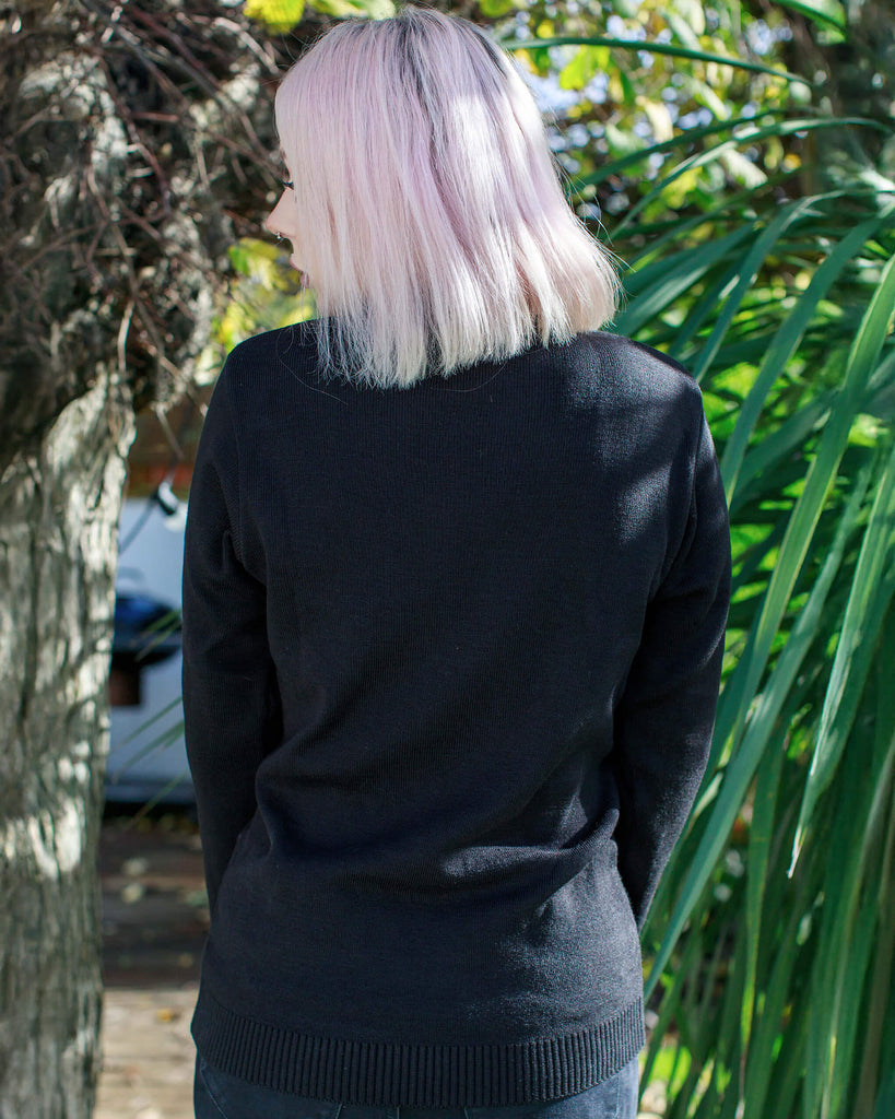 Back view of the daisy chain black jumper on Florence. The black jumper has plain black arms and back with repeating white daisies across the front body.