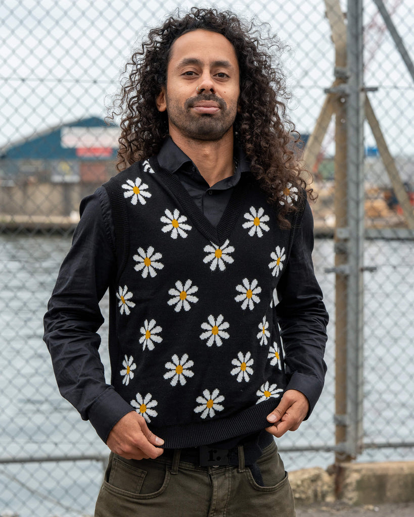 Model Rich wears the Run & Fly Black Daisy Tank Vest featuring white and yellow daisy patterns on a black knit. Styled over a black shirt for a fitted unisex look.