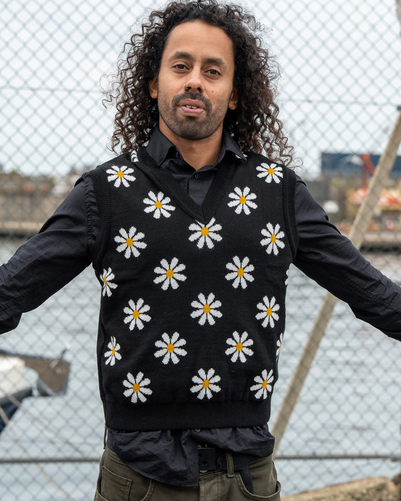 Model Rich poses wearing the Run & Fly Black Daisy Tank Vest layered over a black shirt. The unisex knit features a bright white daisy pattern on black.

