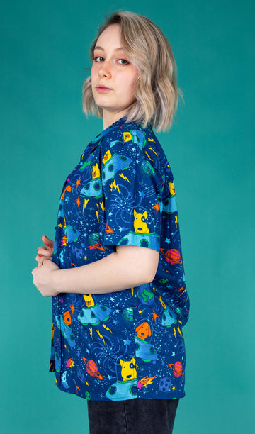 Amy a blonde white femme model with shoulder length hair is wearing a white vest with black jeans and dogs in space blue short sleeved shirt featuring dogs in spaceships, planets, and stars on a blue base