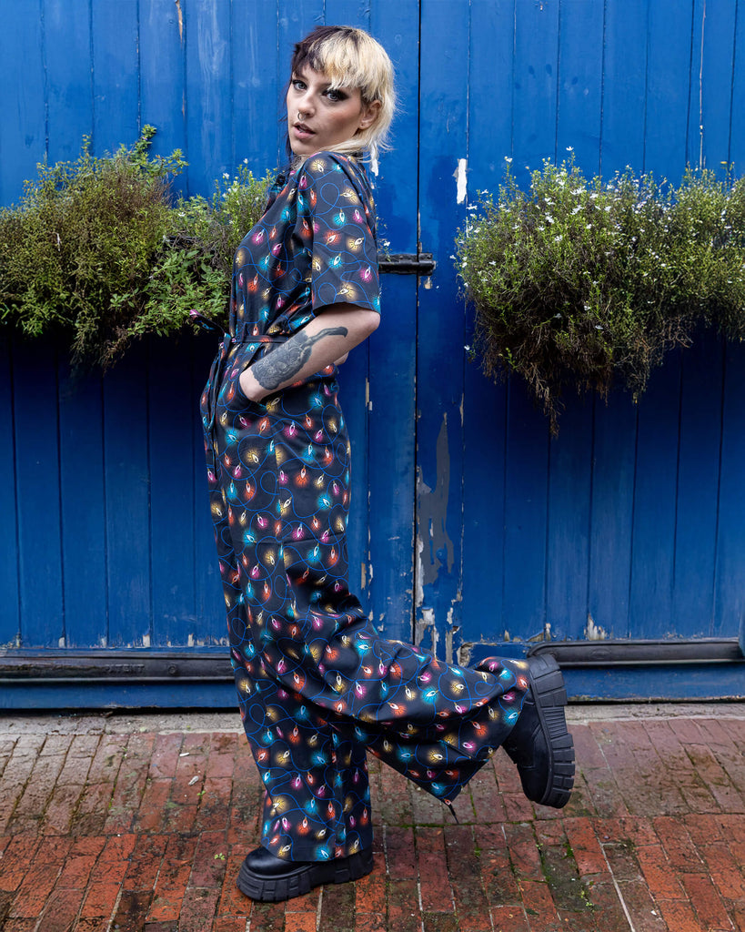 Claudia a model with a half black half blonde mullet is wearing a jumpsuit with fairy lights on stood against a blue door in a mews in hove. 