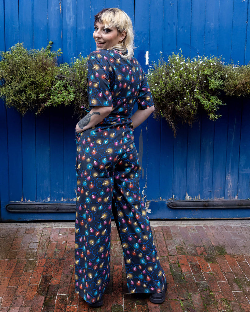 Claudia a model with a half black half blonde mullet is wearing a jumpsuit with fairy lights on stood against a blue door in a mews in hove. 