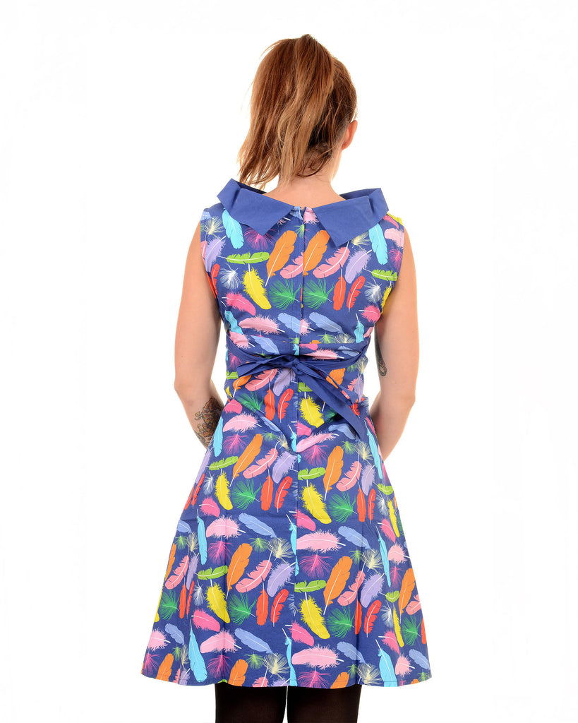 Model is stood in front of a white studio background wearing the feather 60's dress with tights underneath. They are facing away from the camera with both hands in front of them. Photo is cropped from the knees up.