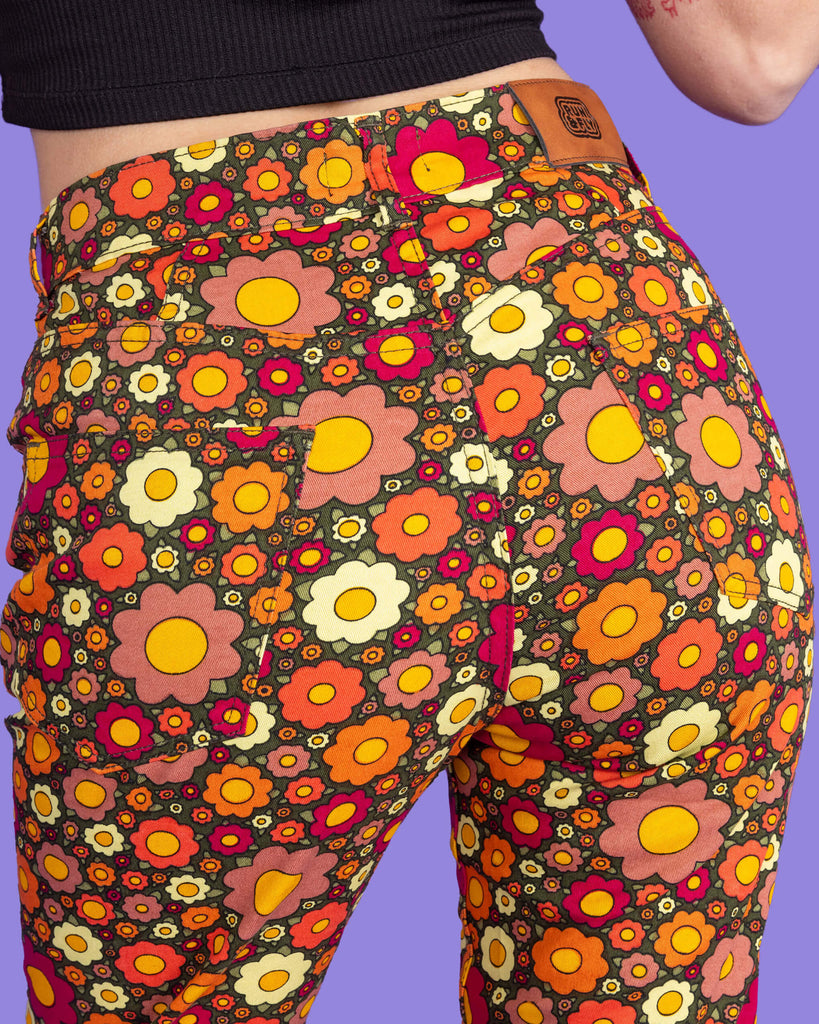 Close up of Ditsy Floral Bell Bottom Flares. The flares are a dark green colour and covered in red, orange and yellow flowers. Close up shows back pockets and close up of flower print.