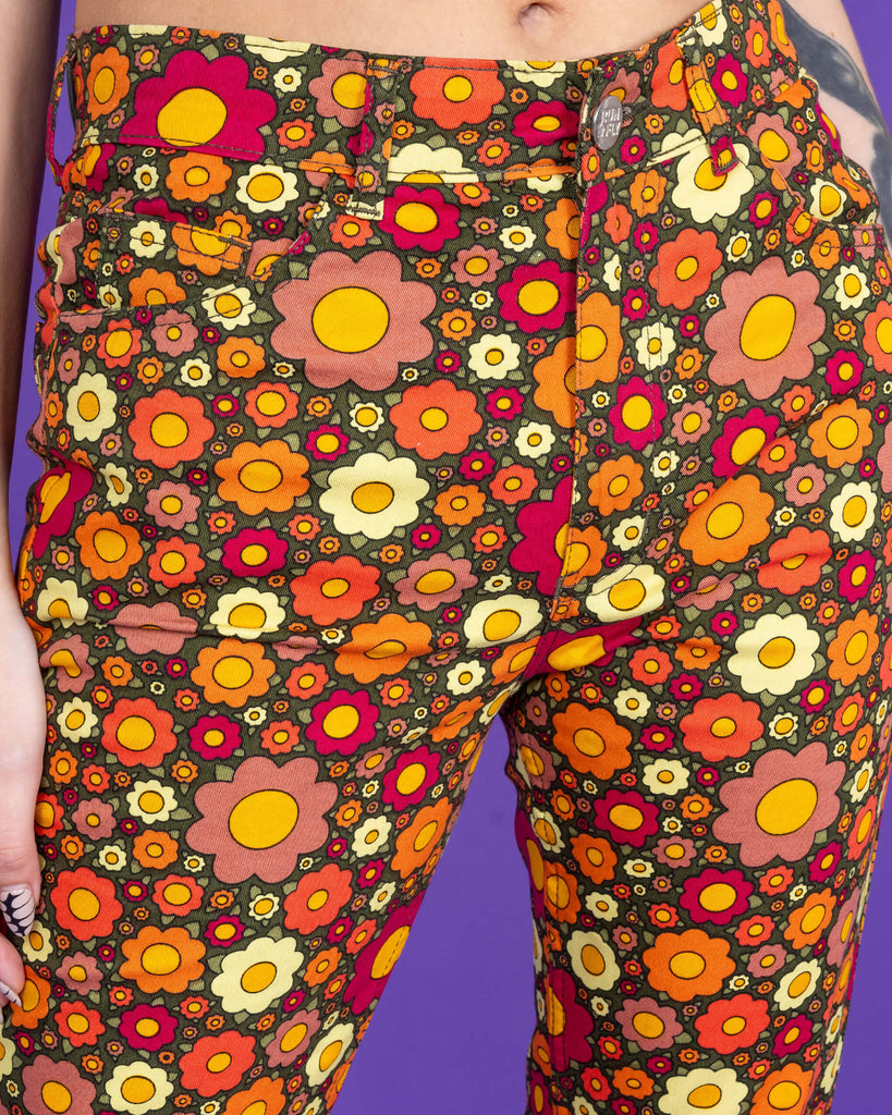 Close up of Ditsy Floral Bell Bottom Flares. The flares are a dark green colour and covered in red, orange and yellow flowers. Close up shows the front pockets and a close up of the flower print.