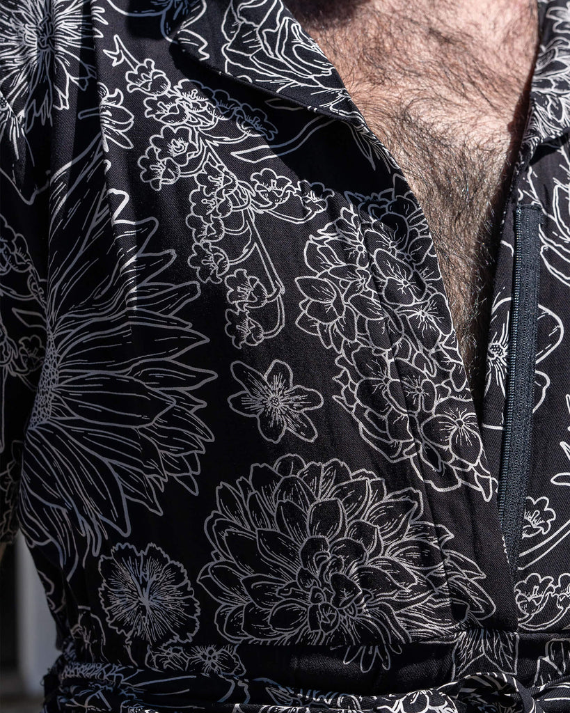 Close up of the Black and White Floral Rayon Jumpsuit zip up front and belt tie detailing worn by a masc non binary person. The black base jumpsuit features white floral outlines all over.