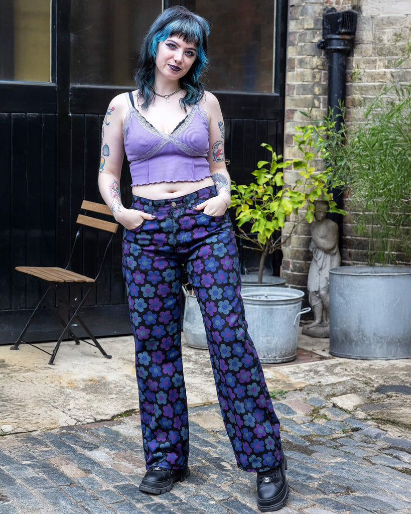 Faeryn a femme non binary person with blue and black hair and dark make up is wearing floral jeans and lilac top in a Hove mews 