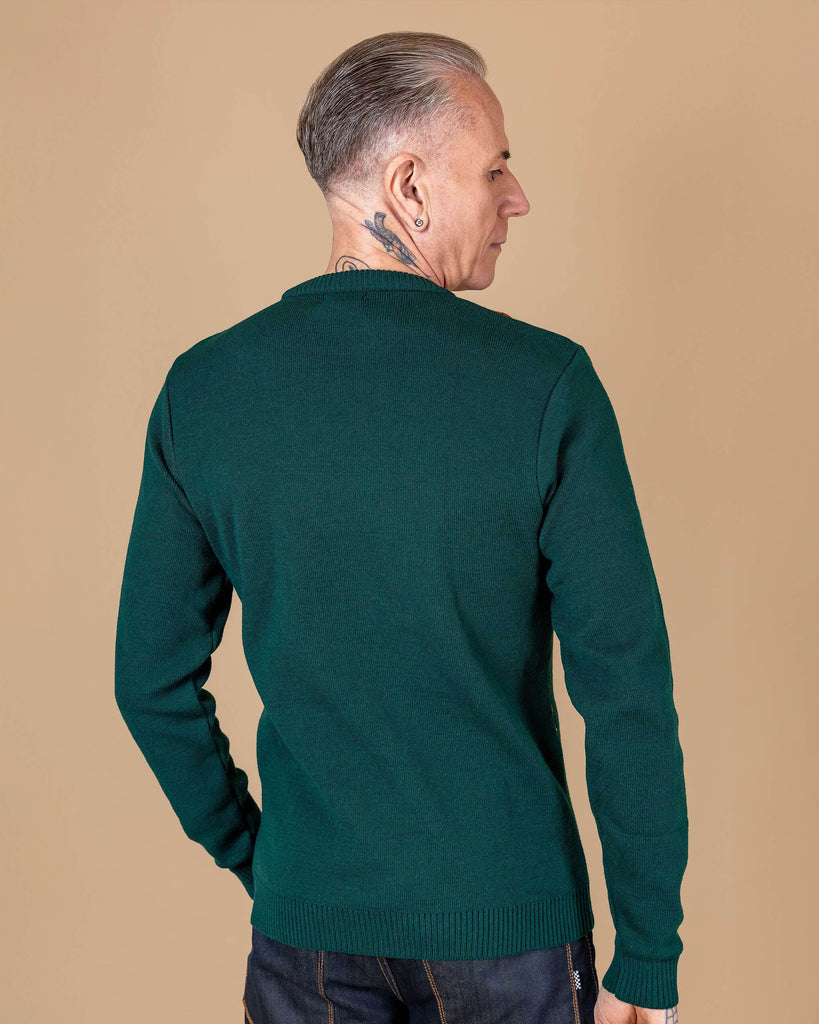 a white male tattooed model is stood in front of a beige backdrop wearing Forest Green Fox Head Jumper paired with jeans. The model is stood with his back to the camera to show the plain green back side of the jumper. 