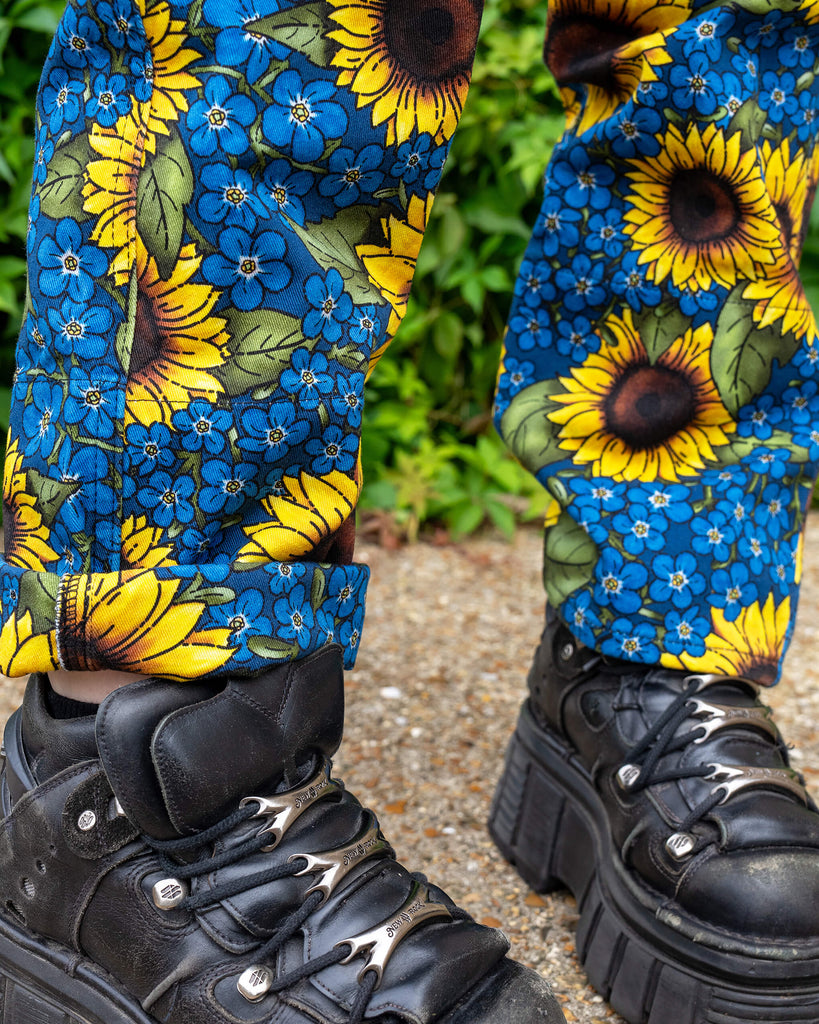 Close up of Run & Fly x Jen James Design Forget Me Not Charity High Waist Straight Leg Jeans. The print is an all over bright yellow sunflower and blue forget me not floral design. The close up shows the matching turn-ups on the jeans with chunky black boots underneath.