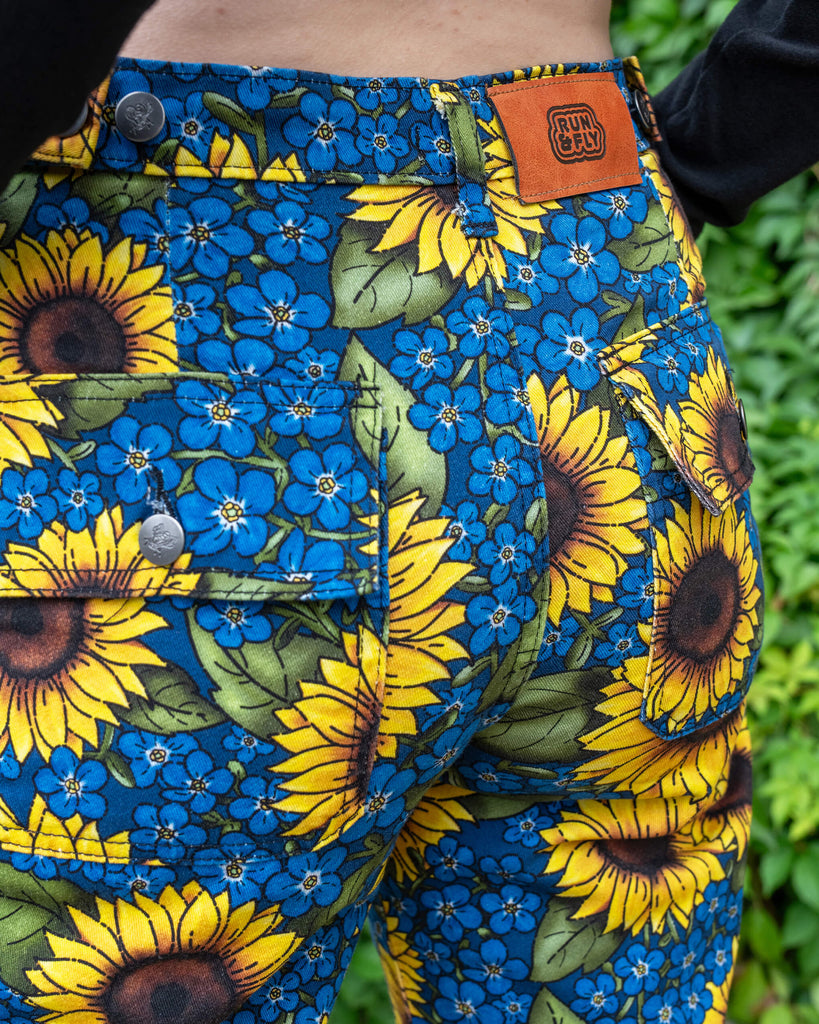 Close up of Run & Fly x Jen James Design Forget Me Not Charity High Waist Straight Leg Jeans. The print is an all over bright yellow sunflower and blue forget me not floral design. The close up shows the back pockets and Run & Fly logo at the back of the jeans.