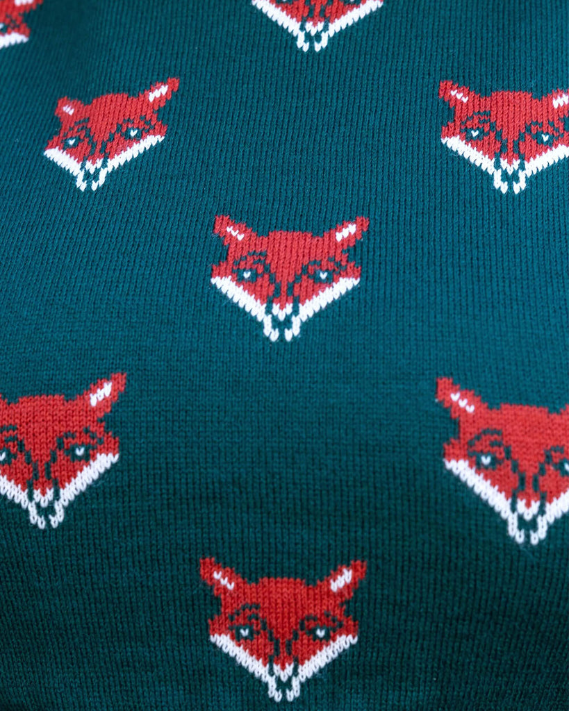 Close up of the fox head green knitted tank top modelled by Charlotte. The knitted tank top is a bottle green colour with various orange and white fox heads all over and a plain green back.