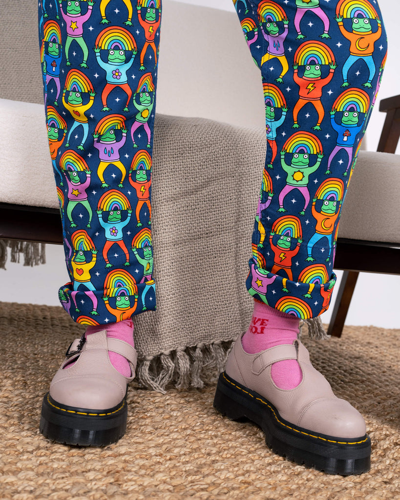 Focus on the legs of the Run & Fly Rainbow Frogs Stretch Twill Dungarees, styled with pink socks and chunky shoes. The playful frog and rainbow print pops against the navy fabric. Ethically made.