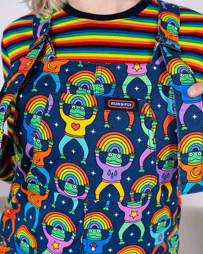 Close-up of the chest area of Run & Fly Rainbow Frogs Stretch Twill Dungarees. The design highlights colourful cartoon frogs with rainbow halos and quirky details on a navy backdrop. Ethical and unique.