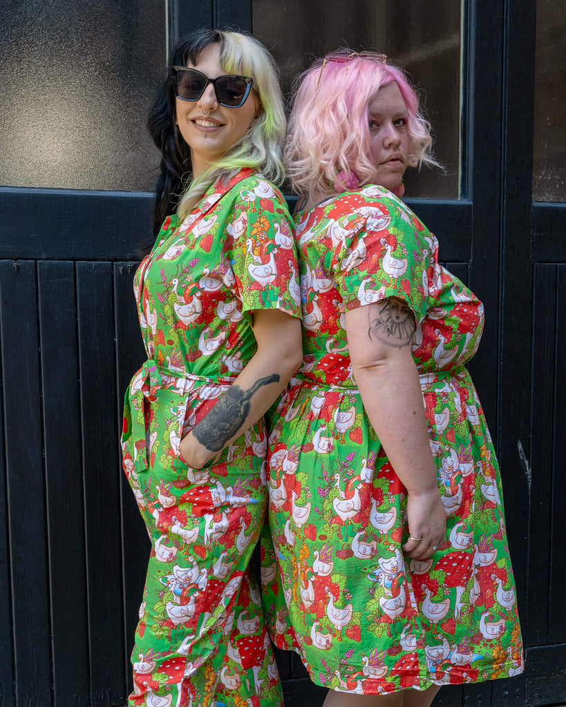 Two models pose back-to-back, both wearing outfits with the same vibrant geese and garden print. One wears a jumpsuit, and the other a dress, both from Run & Fly, an ethical slow fashion brand. Their playful and stylish outfits are perfect for eco-conscious fashion lovers.