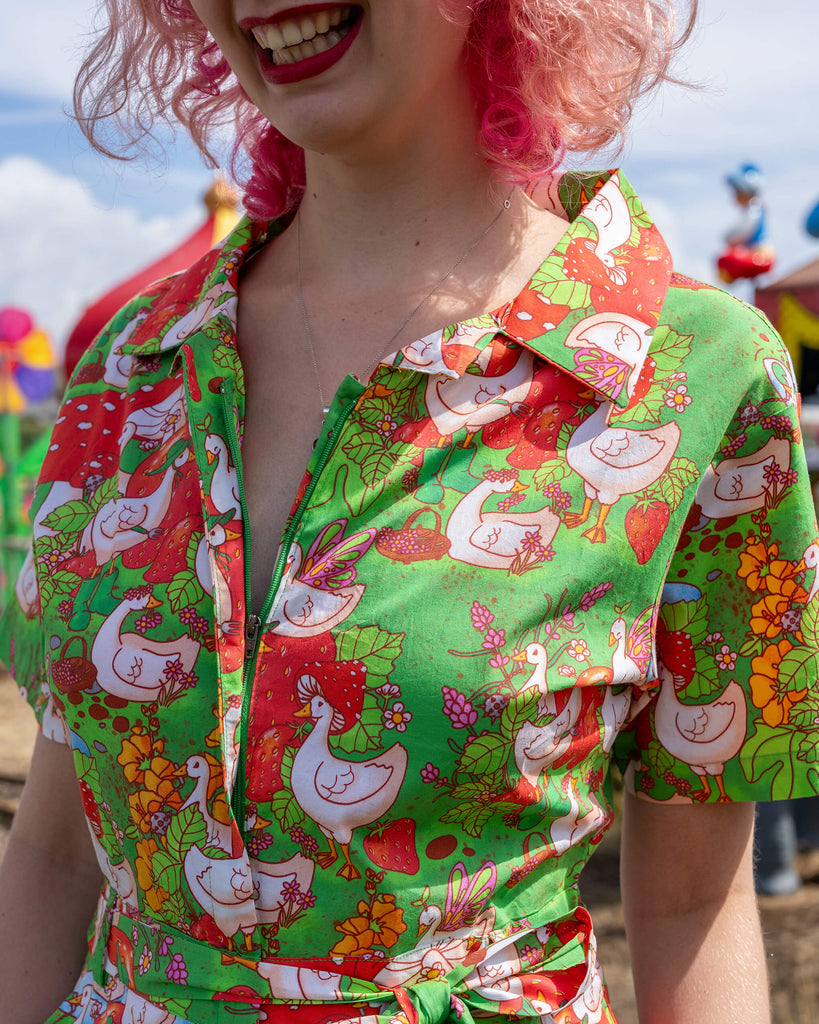 A close-up of a collar and neckline of a bright green jumpsuit from Run & Fly, featuring a whimsical pattern of geese, mushrooms, and strawberries. The fun and bold design adds charm to the brand’s ethical slow fashion ethos.