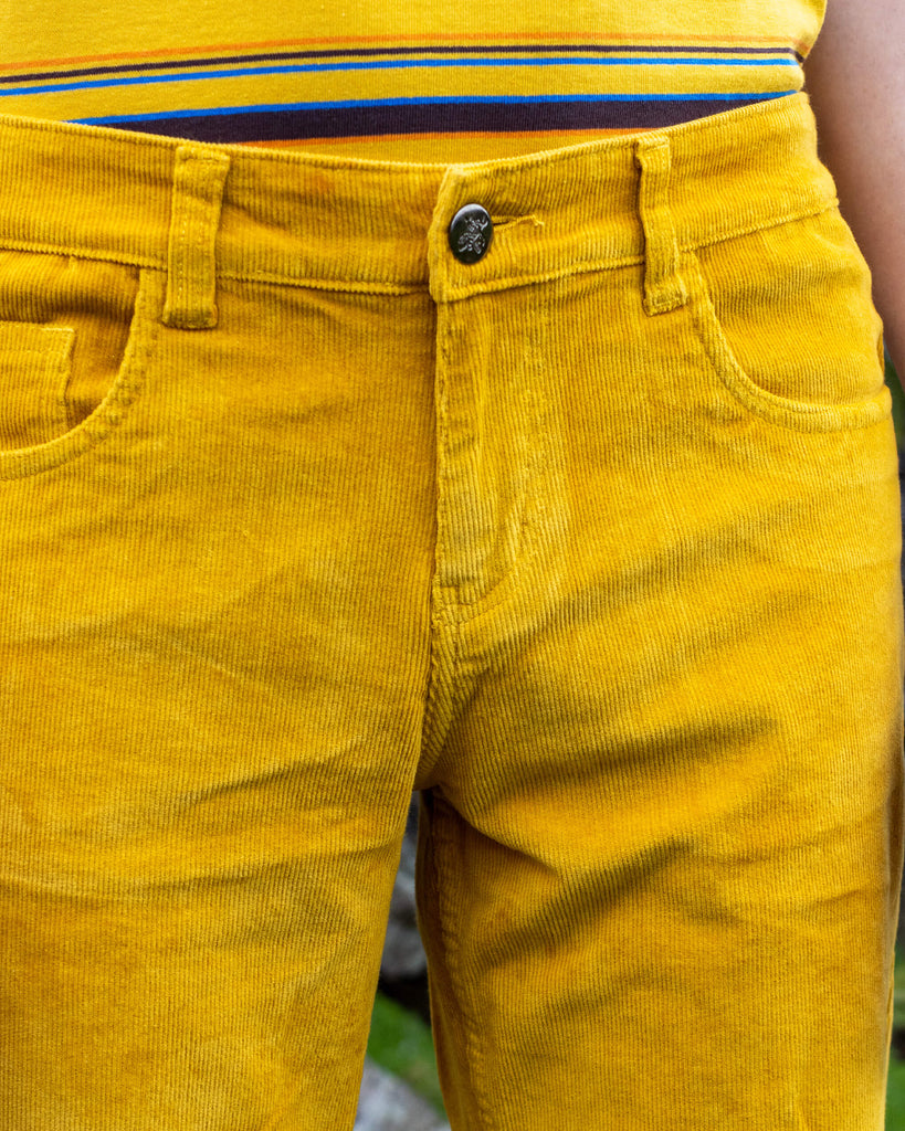  Close-up of the front of Run & Fly’s Gold Corduroy Flares on model Jack, showcasing the textured fabric and detailing around the waistband and pockets. The golden hue is warm and eye-catching.