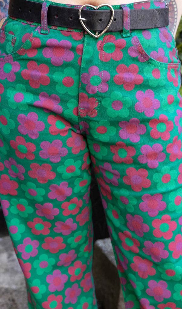 Faeryn a femme non binary person with blue and black hair and dark make up is wearing floral jeans and lilac top in a Hove mews this is a close up of the trousers