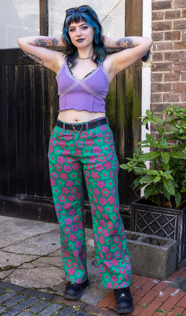 Faeryn a femme non binary person with blue and black hair and dark make up is wearing floral jeans and lilac top in a Hove mews 