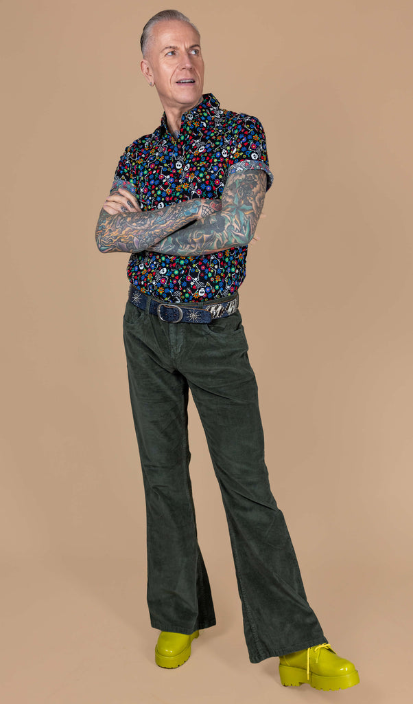 James is stood in front of a beige background wearing the forest green corduroy bell bottom flares with the boogie bones shirt and yellow boots. He is stood facing forward leaning back on one leg with his arms crossed and looking off to the right. The flares are mid rise, fitted to thigh and flare at the bottom.