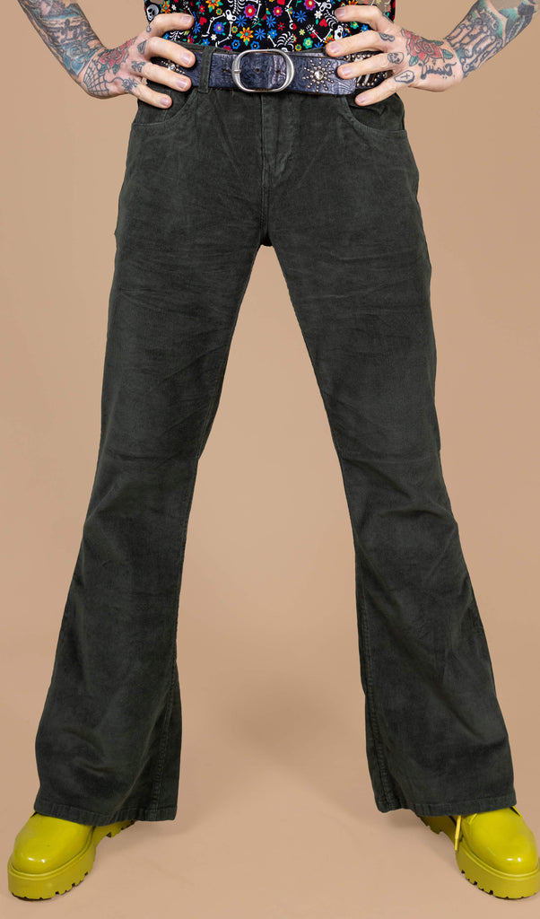 Close up of James wearing the forest green corduroy bell bottom flares with the boogie bones shirt and yellow boots. He is facing forward with his legs stood shoulder width apart and both hands on his hips. The photo is cropped from the hips down.